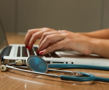 person sitting while using laptop computer and green stethoscope near