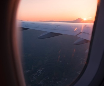 Airplane wing view through window during sunset, capturing a serene sky and landscape below.