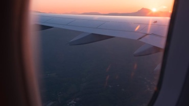 Airplane wing view through window during sunset, capturing a serene sky and landscape below.