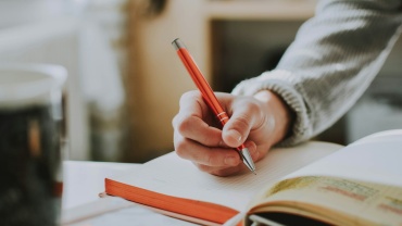 person holding on red pen while writing on book
