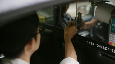 High angle of crop young male passenger in white shirt sitting in automobile and giving dollars to driver