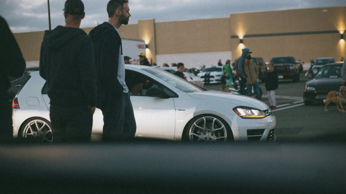 man in black suit standing beside white sedan