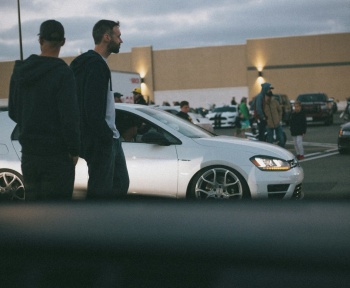 man in black suit standing beside white sedan
