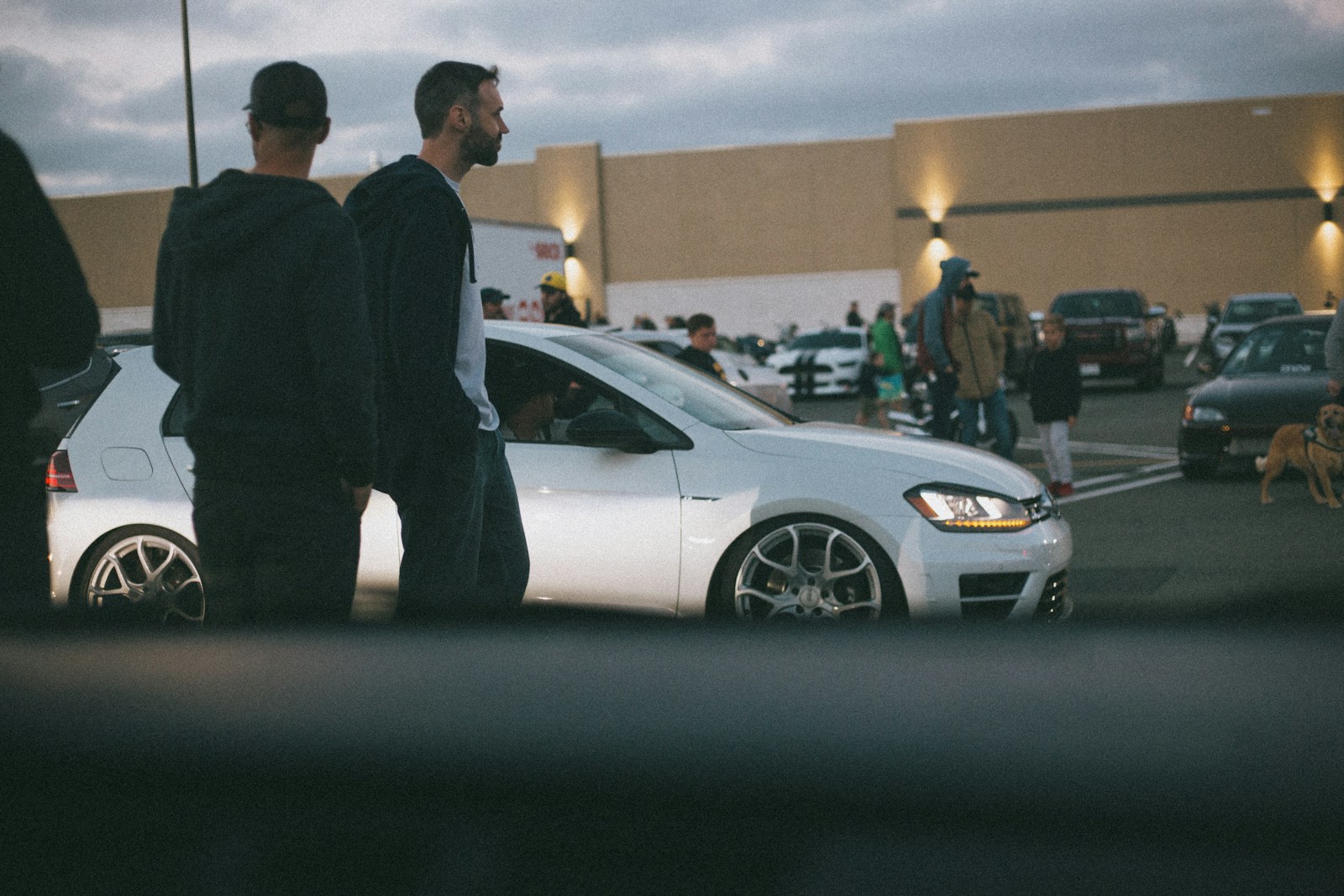man in black suit standing beside white sedan